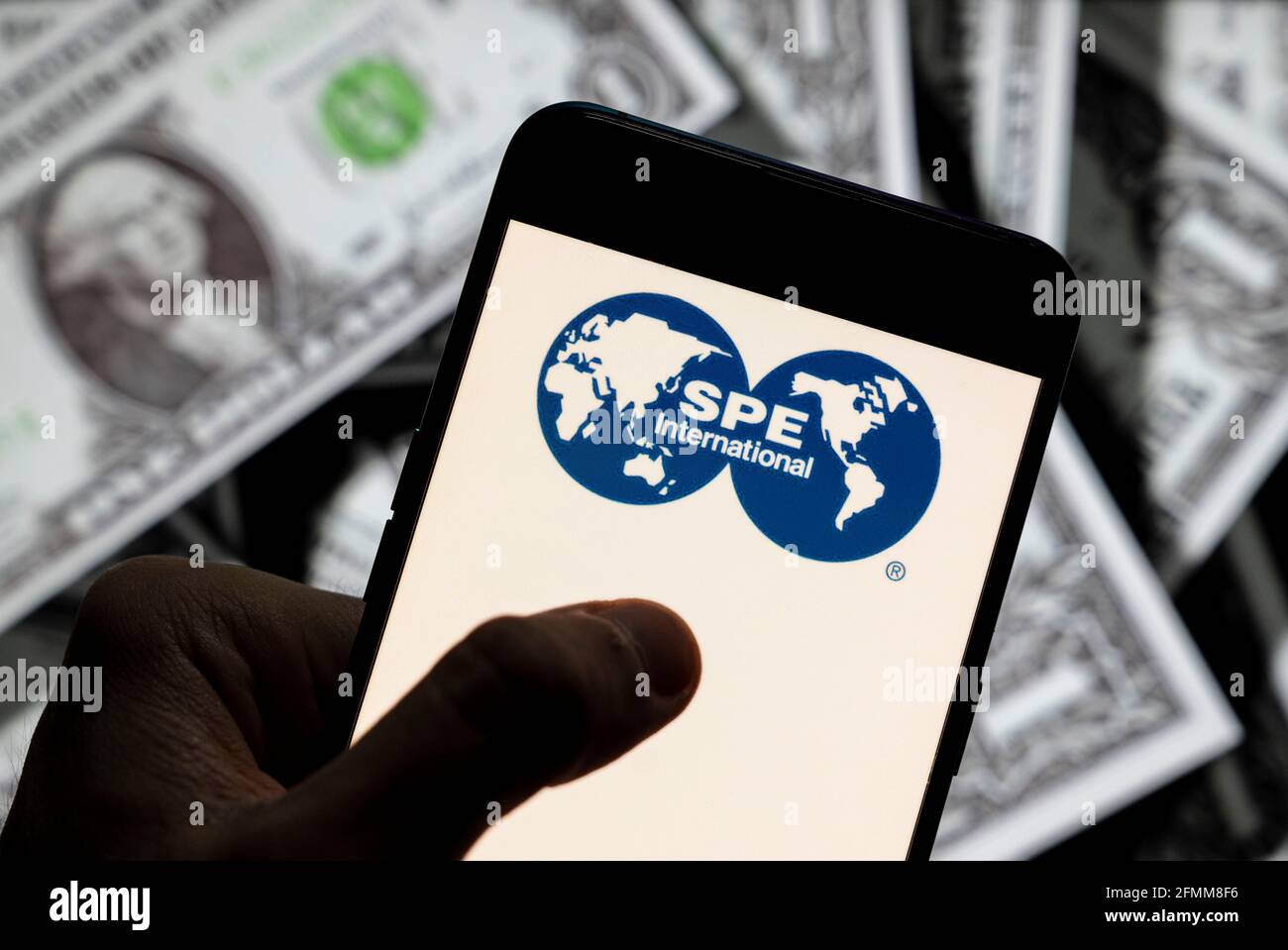 In this photo illustration the Society of Petroleum Engineers (SPE) logo seen displayed on a smartphone with USD (United States dollar) currency in the background. Stock Photo
