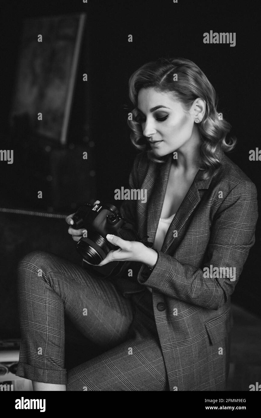 Portrait of a confident beautiful business woman in a suit on a dark background holds a camera in her hands. The concept of gender equality. Strong in Stock Photo