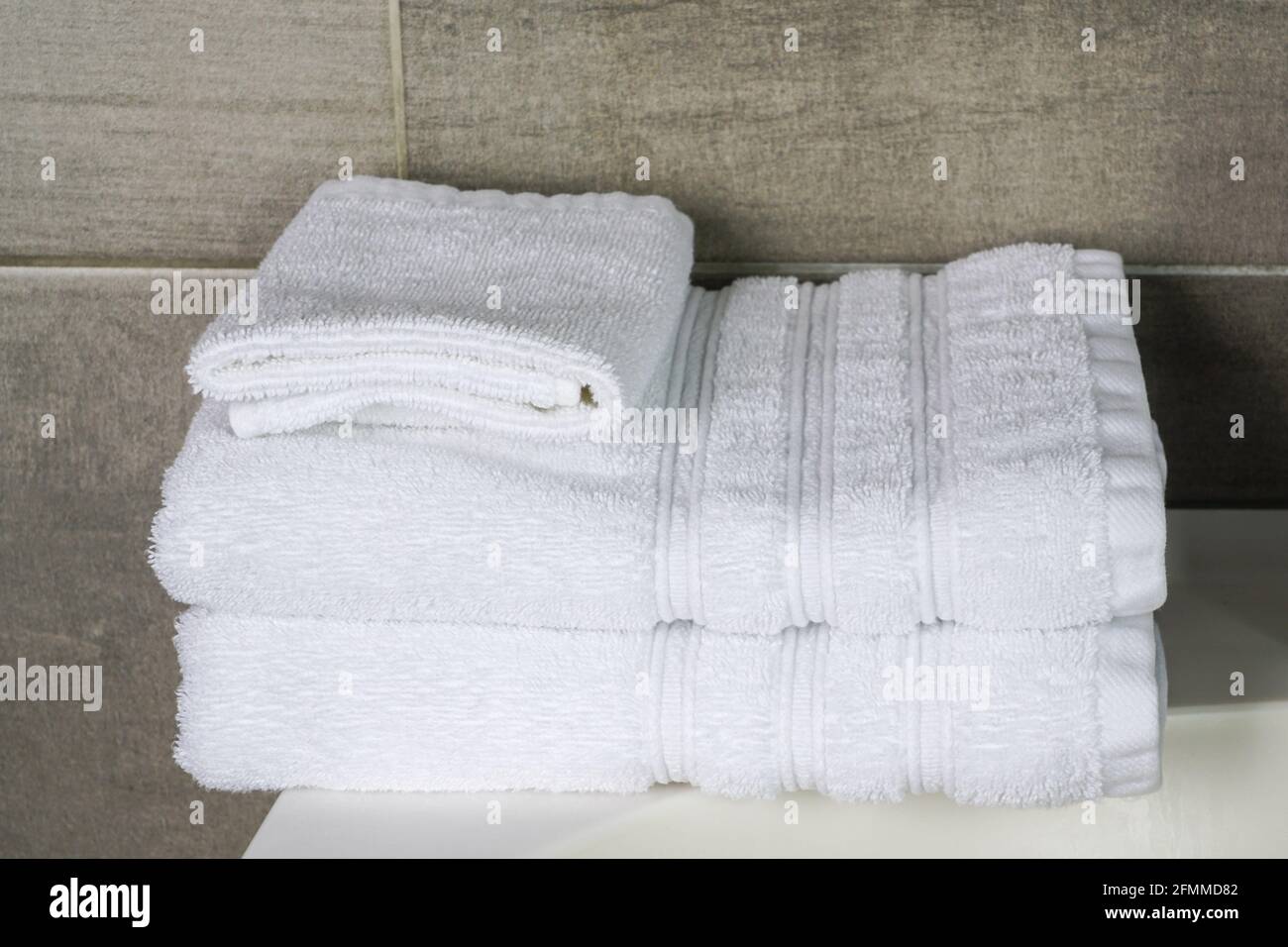 a stack of white clean towels in the hotel bathroom against a gray anthracite tile wall background Stock Photo