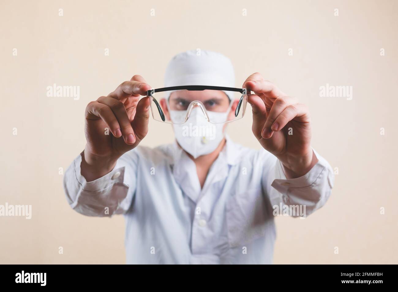 Protective glasses in doctors hands in white lab coat and protective breathing mask defocused on yellow background isolated. Selective focus. Stock Photo