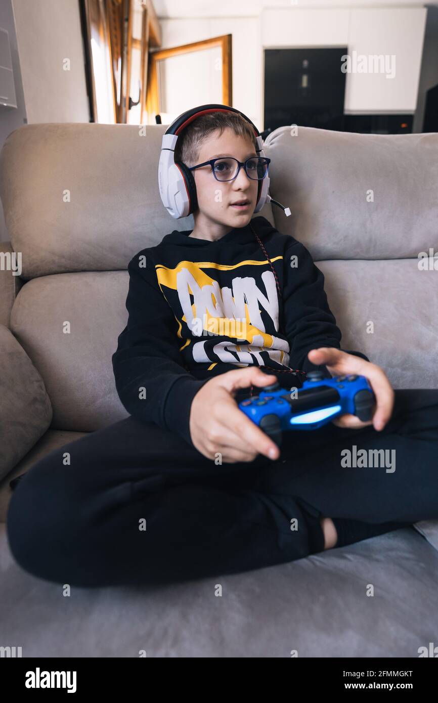 Spanish little boy playing an online videogame sitting on a sofa Stock
