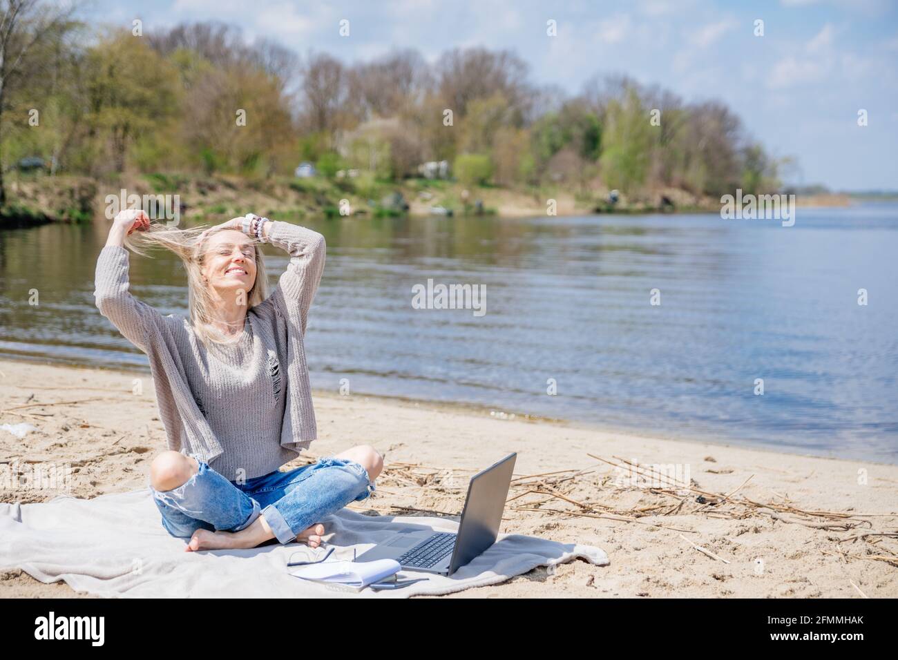 Happy free woman with laptop on the beach by the lake. Stock Photo