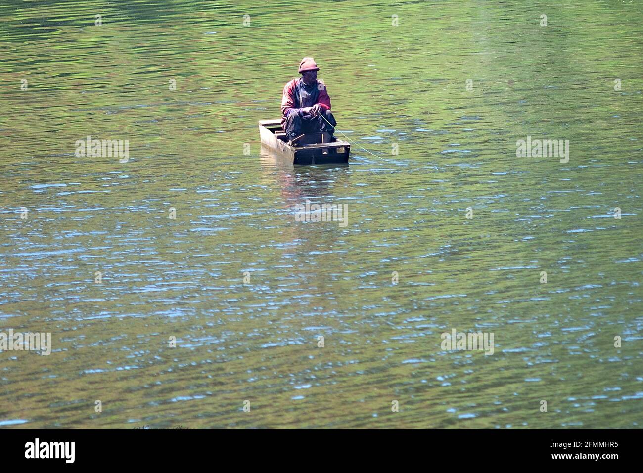 Fisherman sitting huddled in a wooden boat on a pond Stock Photo