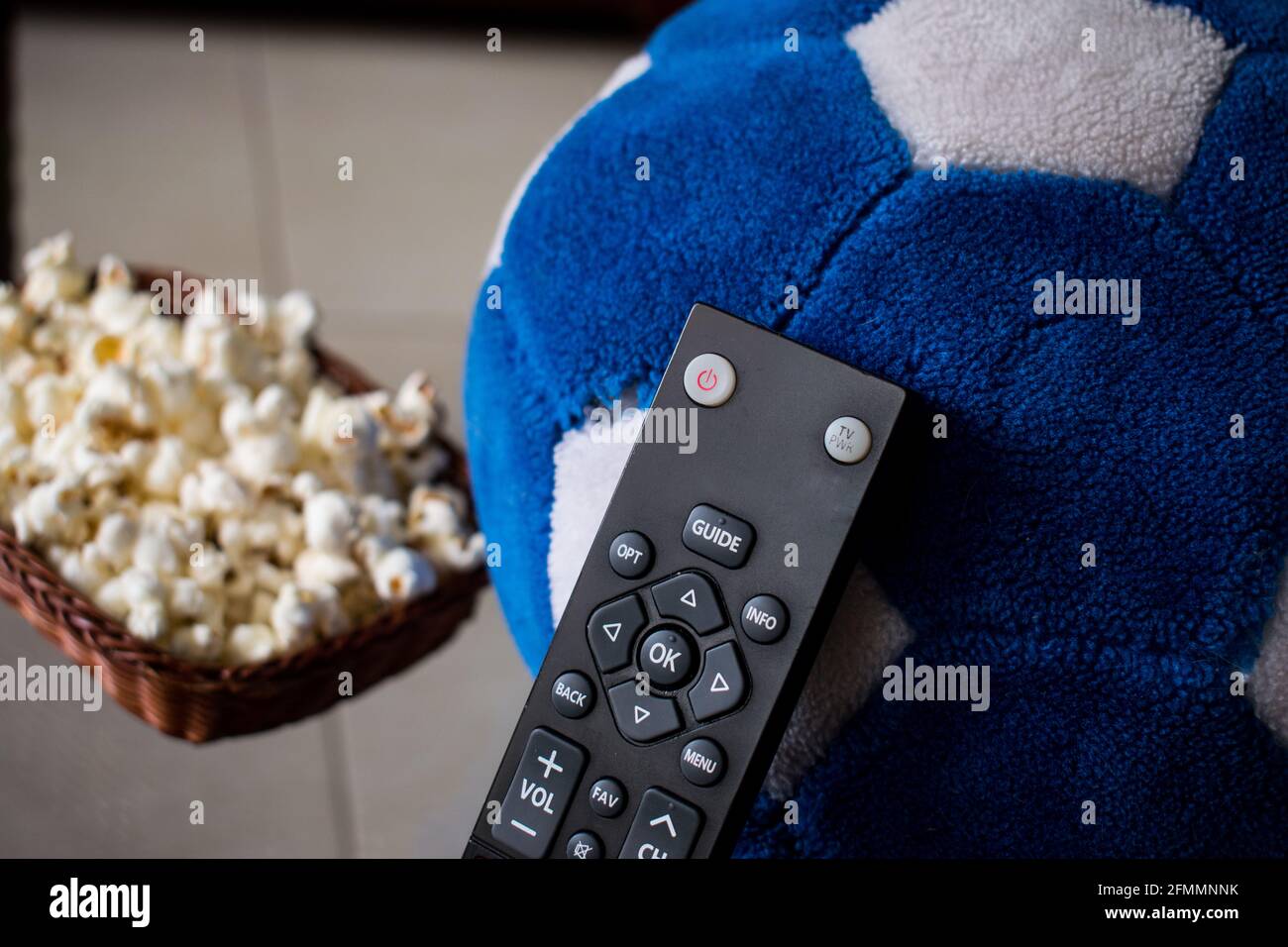 Some pop corn in a basket with a tv control and one soccer ball on a table at home Stock Photo