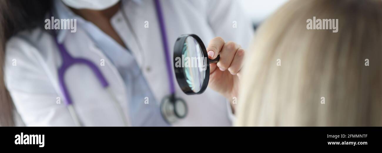 Dermatologist examines patient's face through magnifying glass Stock Photo