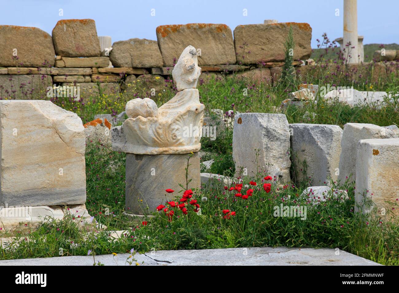 Close up of carved marble column base with ruins and wildflowers, island of Ancient Delos, Greek archipelago, Greece Stock Photo