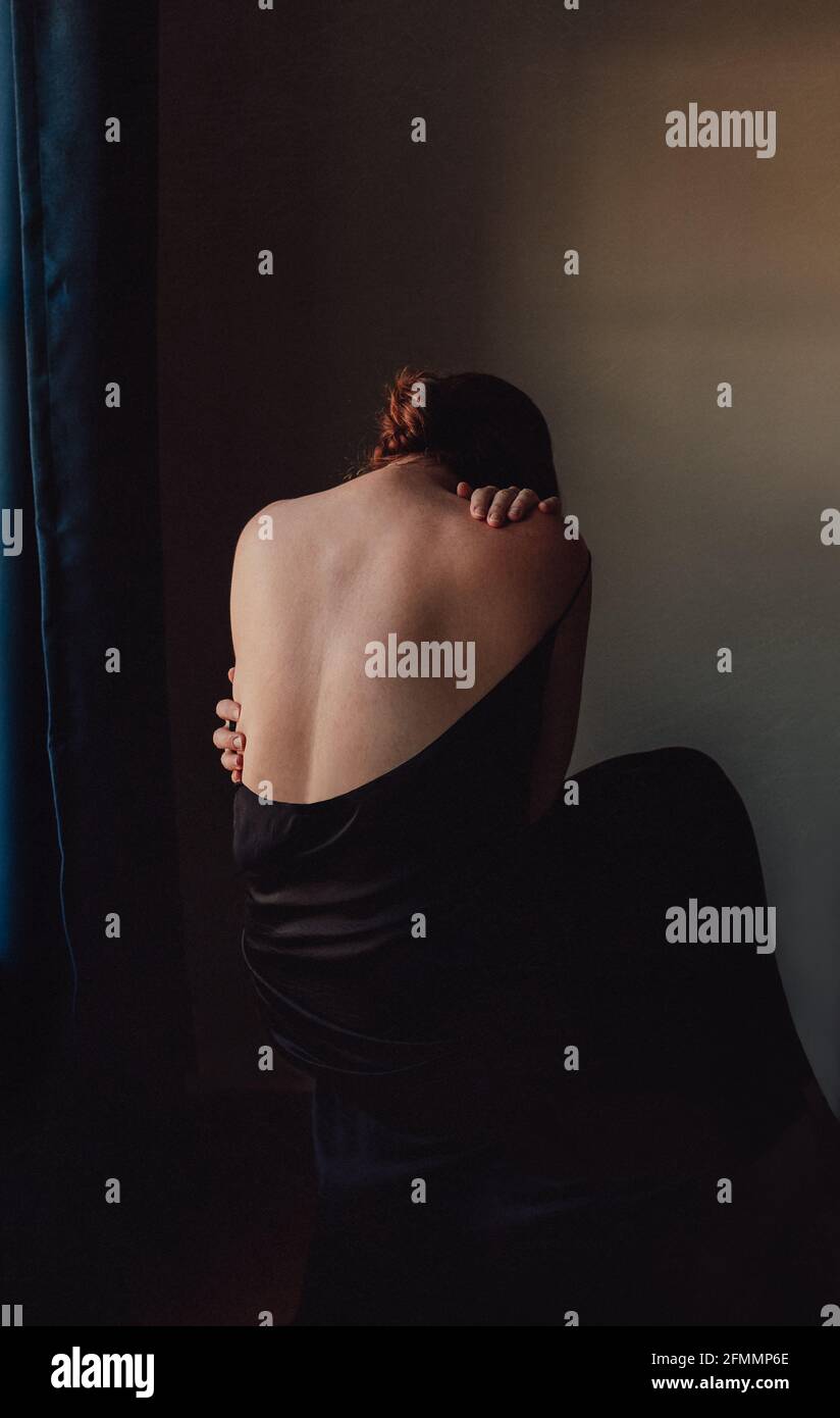 Back view of sad woman bent forward with back exposed in a dark room. Stock Photo