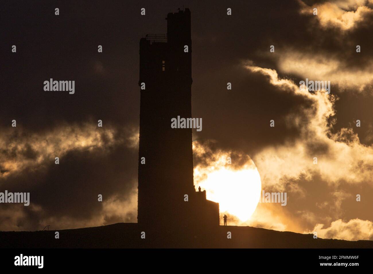 People watch the sun set over Victoria Tower, Castle Hill, Huddersfield
