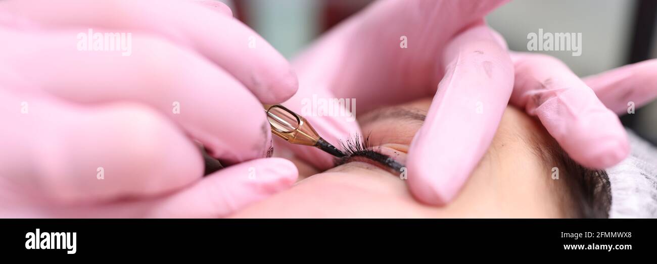 Master performs permanent makeup on eyelids by making decorative arrow Stock Photo