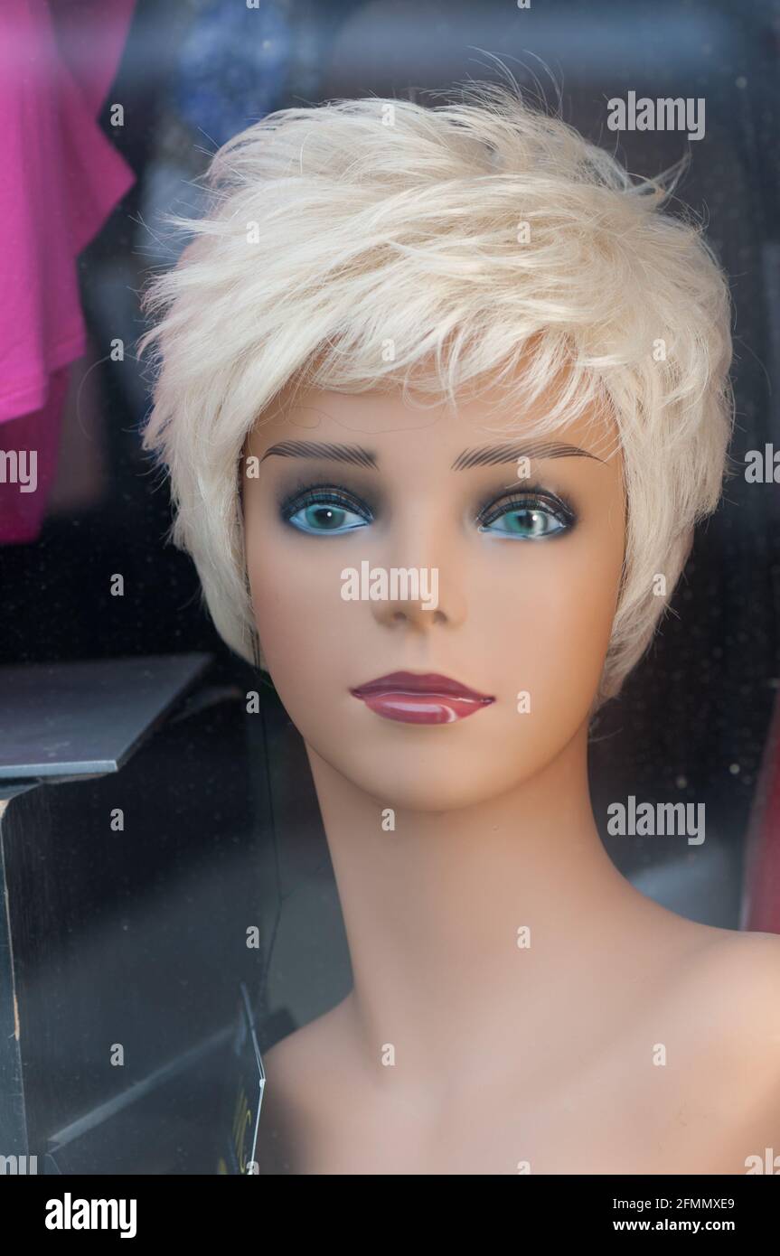 wig seller, feat. a Caucasian female with piercing blue-green eyes and a short stylish blond wig - or plastic mannequin with blond wig in a shop Stock Photo