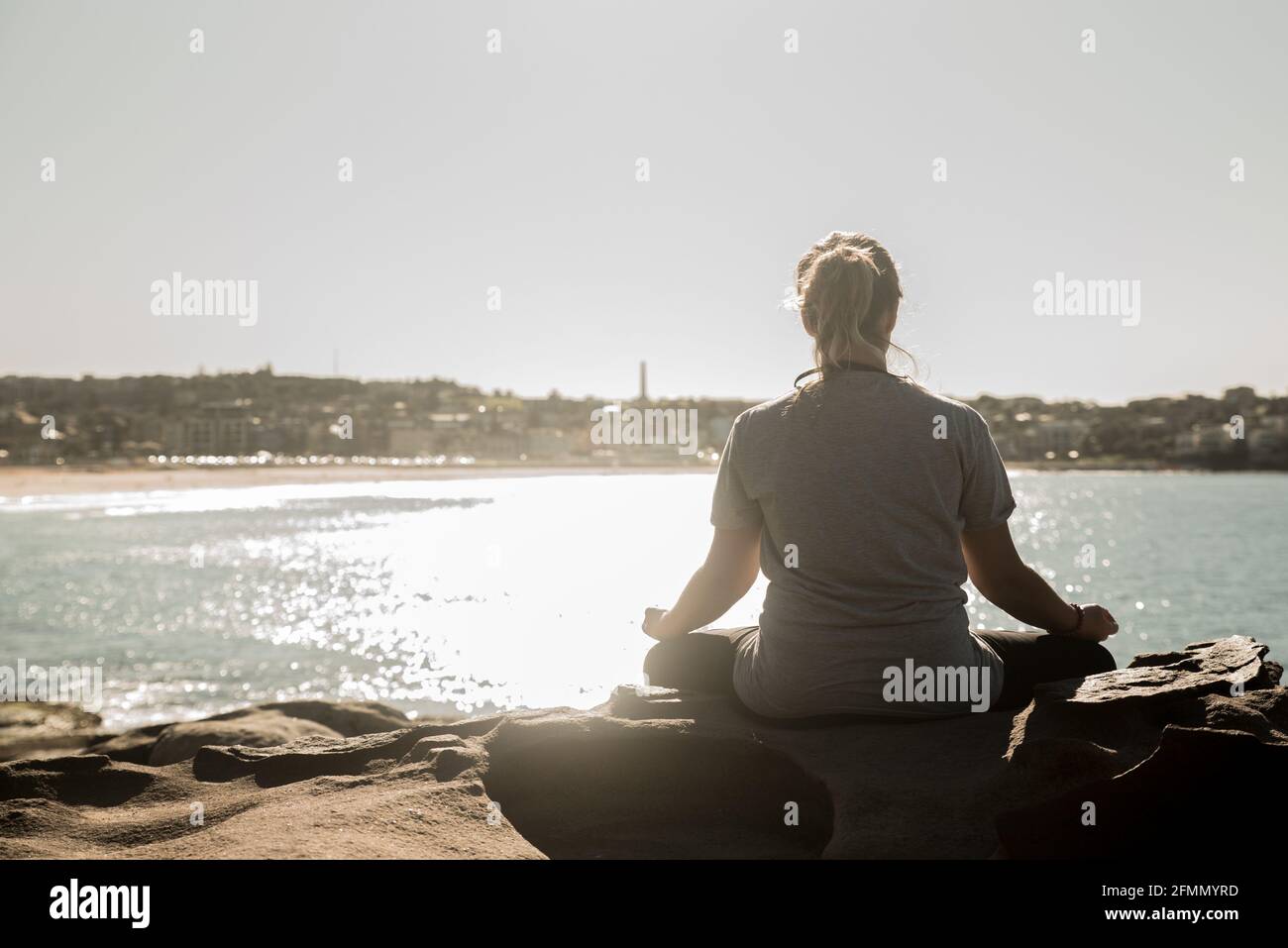 Sunset in Bondi Beach where a young woman with back makes a yoga position Stock Photo