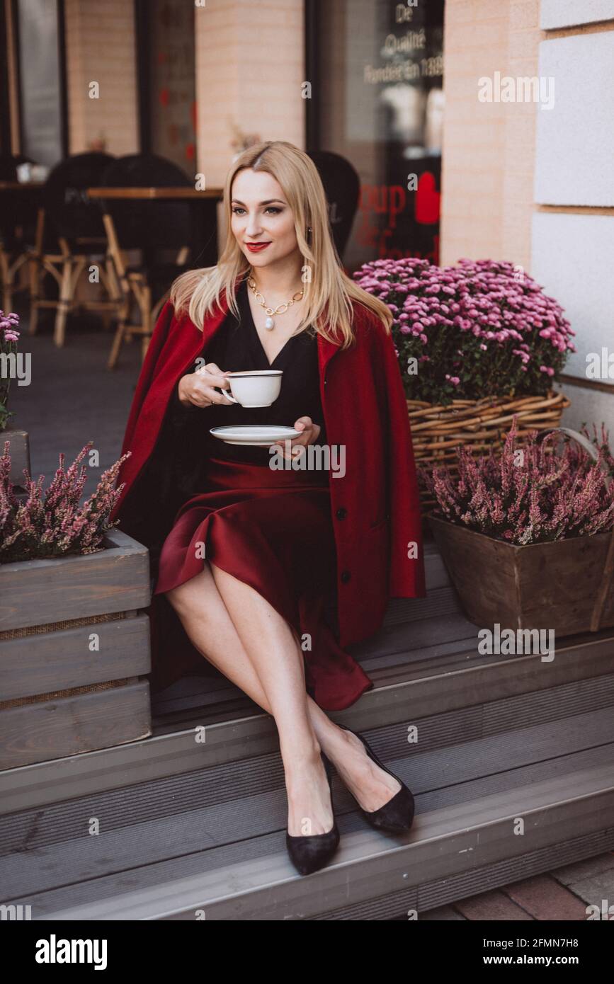 Beautiful young blonde woman in a trendy autumn outfit in burgundy marsala color with a cup of coffee on the steps of a cafe. Soft selective focus. Ar Stock Photo - Alamy Beautiful young blonde woman in a trendy autumn outfit in burgundy marsala color with a cup of coffee on the steps of a cafe. Soft selective focus. Ar Stock Photo - Alamy