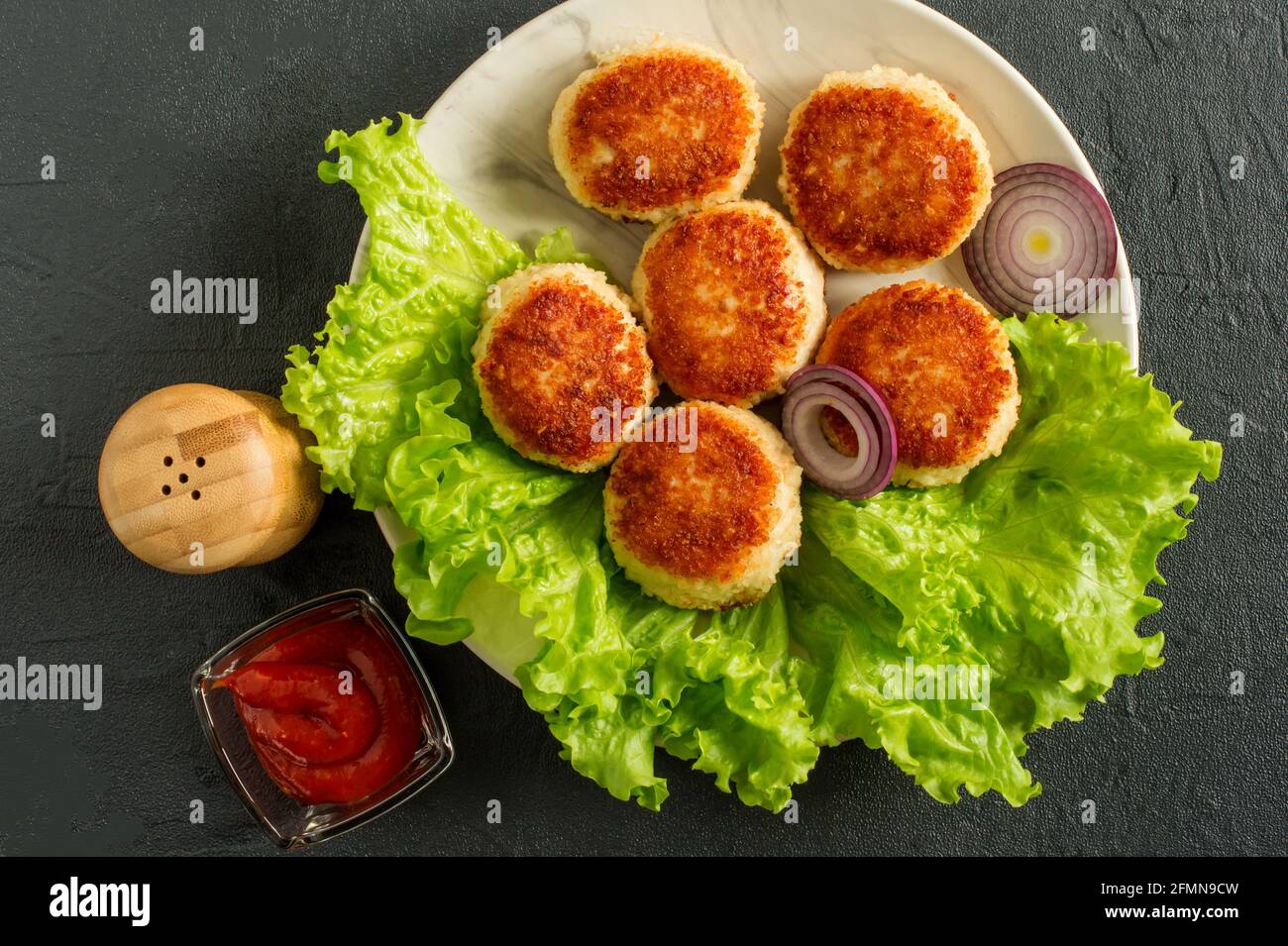 juicy delicious coated with breadcrumbs and fried chicken cutlets on white plate with spices and cetchup on dark background, view from above. Stock Photo