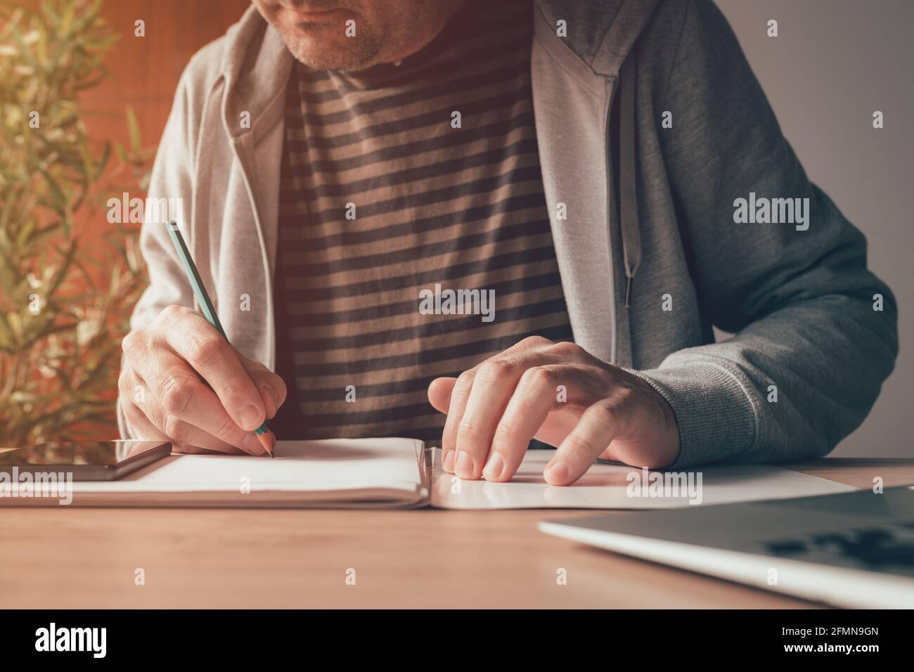 Freelance worker writing notes at home office desk, close up with selective focus Stock Photo