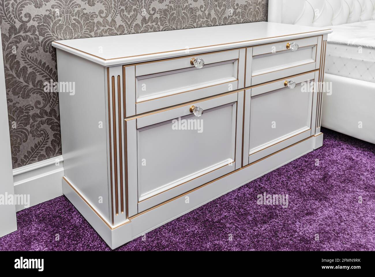 Classical bedside table with drawers and crystal handles on a bright purple carpet Stock Photo