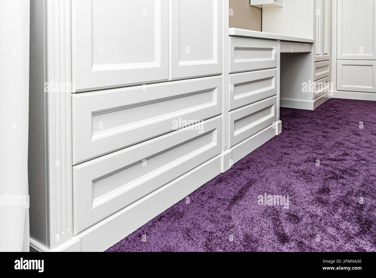 Classical style wardrobe with writing desk and drawers on a bright purple carpet in a bright room low angle view Stock Photo