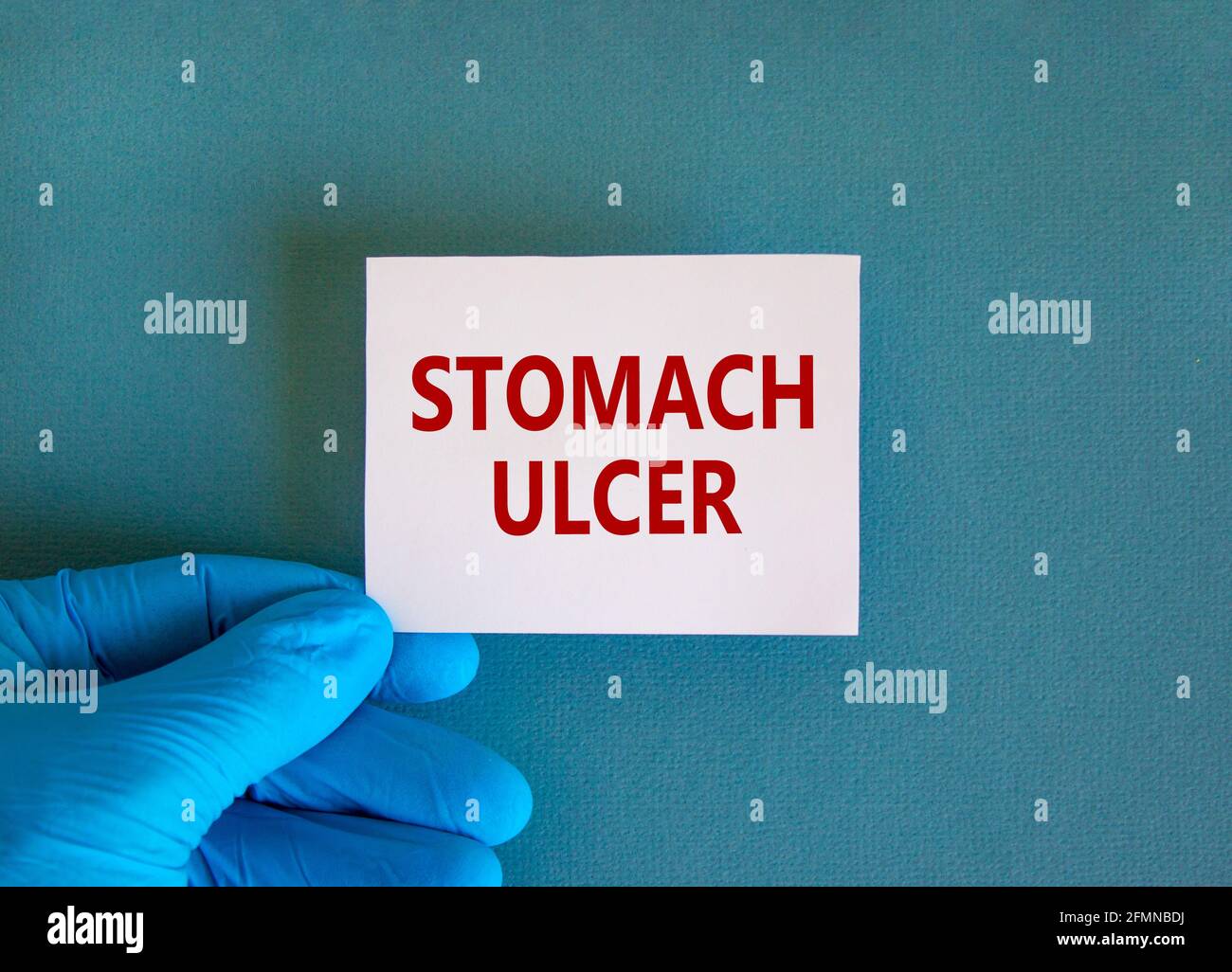 Medical and stomach ulcer symbol. Doctor hand. White card with words 'stomach ulcer'. Beautiful blue background. Doctor hand in blue glove. Medical an Stock Photo