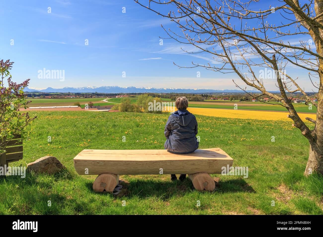 Middle age woman sitting on wooden bench on a viewpoint in the Chiemgau area with view to the alps Stock Photo