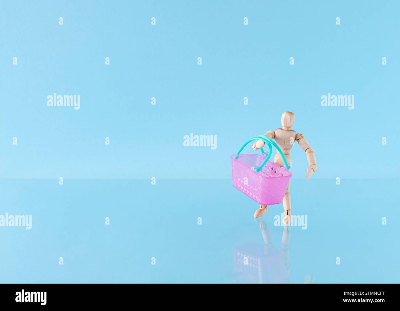 Creative layout with a wooden mannequin with a pink basket on the blue background. Concept of buying and selling of goods or services using the intern Stock Photo