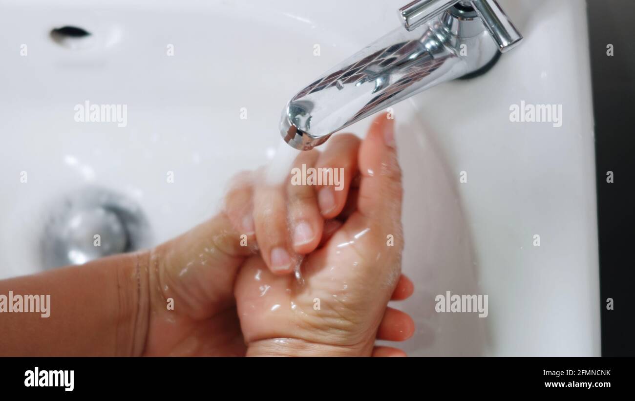 Closeup young woman hands using soap and washing hands under the water ...