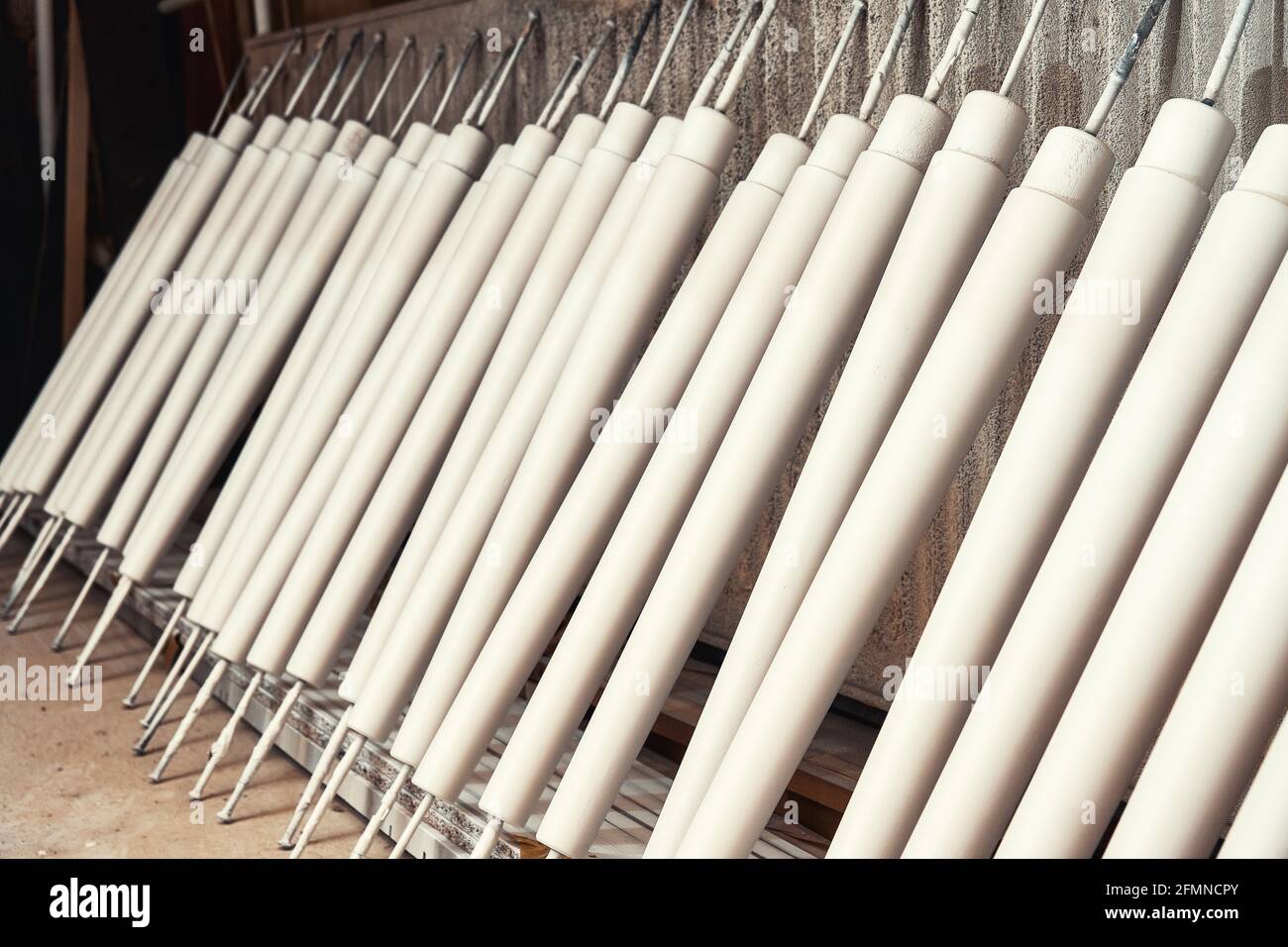 Collection of new wooden furniture legs drying after applying paint leaned on large rack in light woodwork shop close view Stock Photo