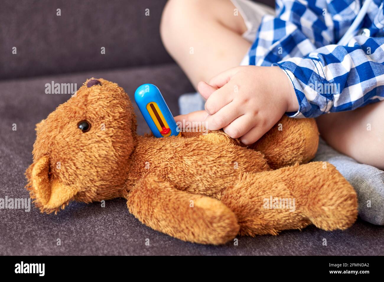 A little boy measures the temperature of a teddy bear with a toy