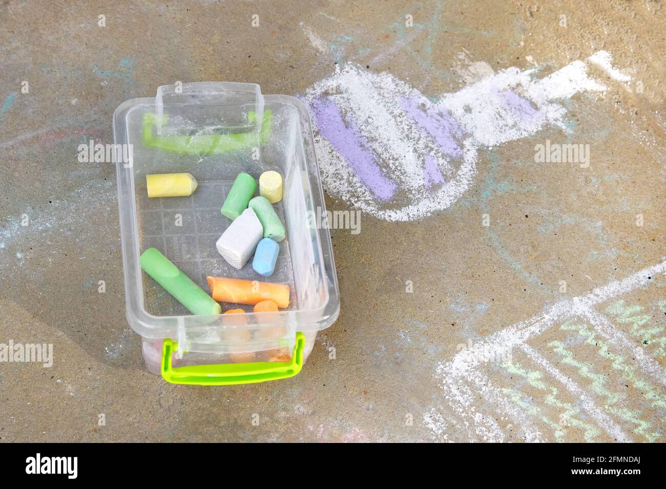 Crayons of blue, green, yellow, white in plastic box. Painted with colored crayons floor tiles in park. Childrens drawing on sidewalk. Childrens leisu Stock Photo