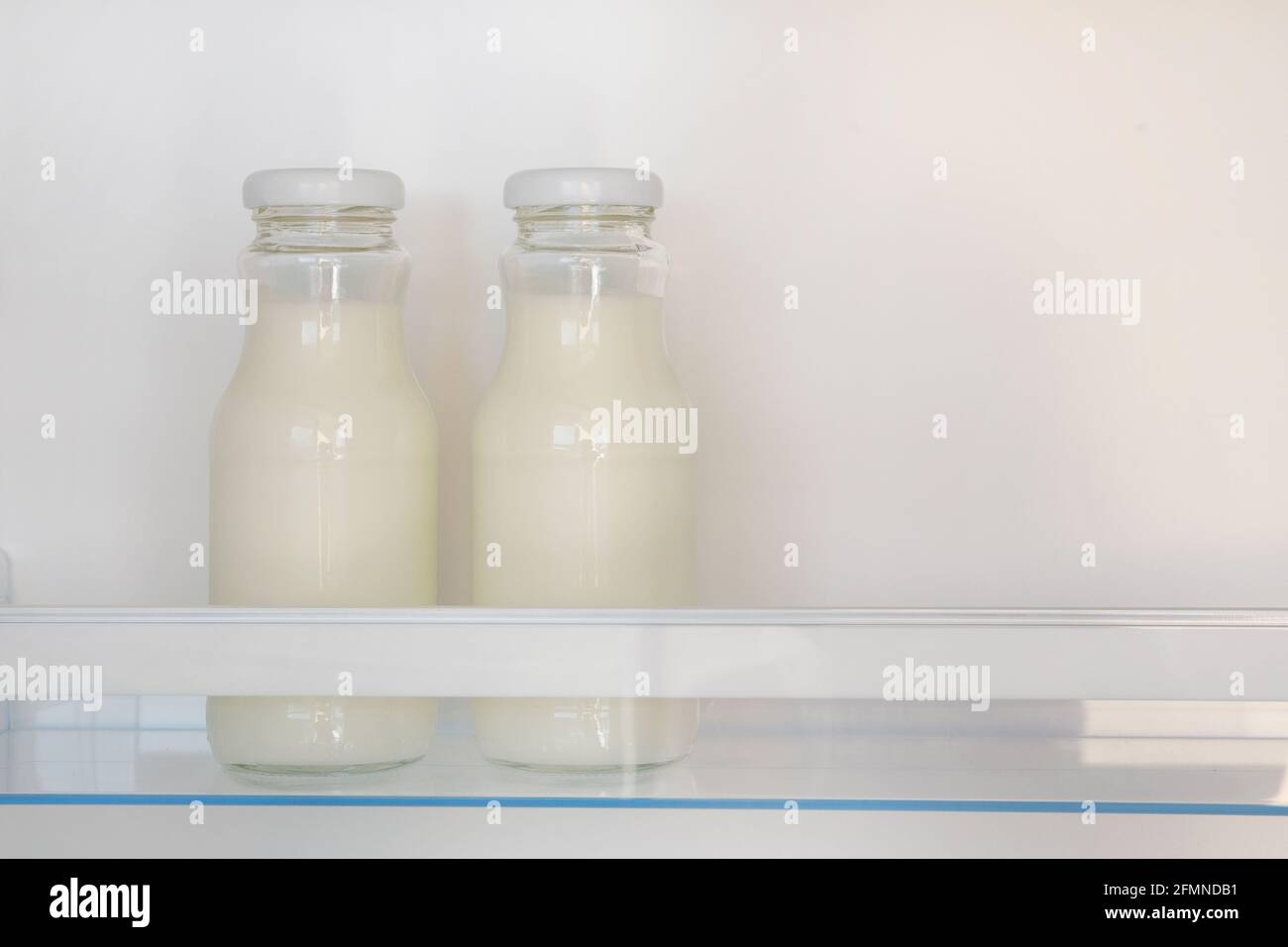 Dairy products in glass bottles on shelf of open empty fridge. White milk in  refrigerator. Horizontal view with copy space. Stock Photo