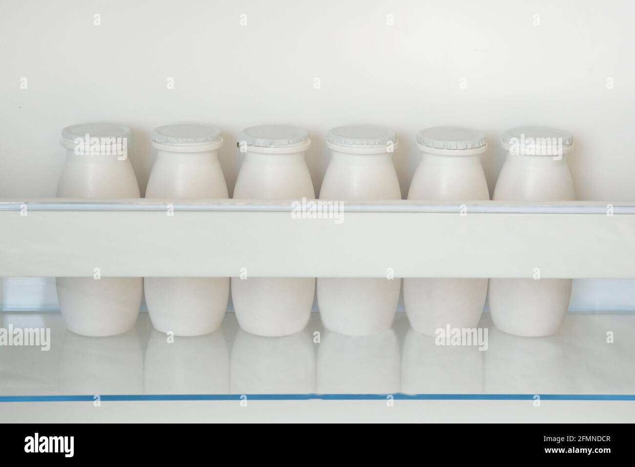White bottles of yoghurt on shelf of open empty fridge. Weight loss diet concept. Horizontal view. Stock Photo