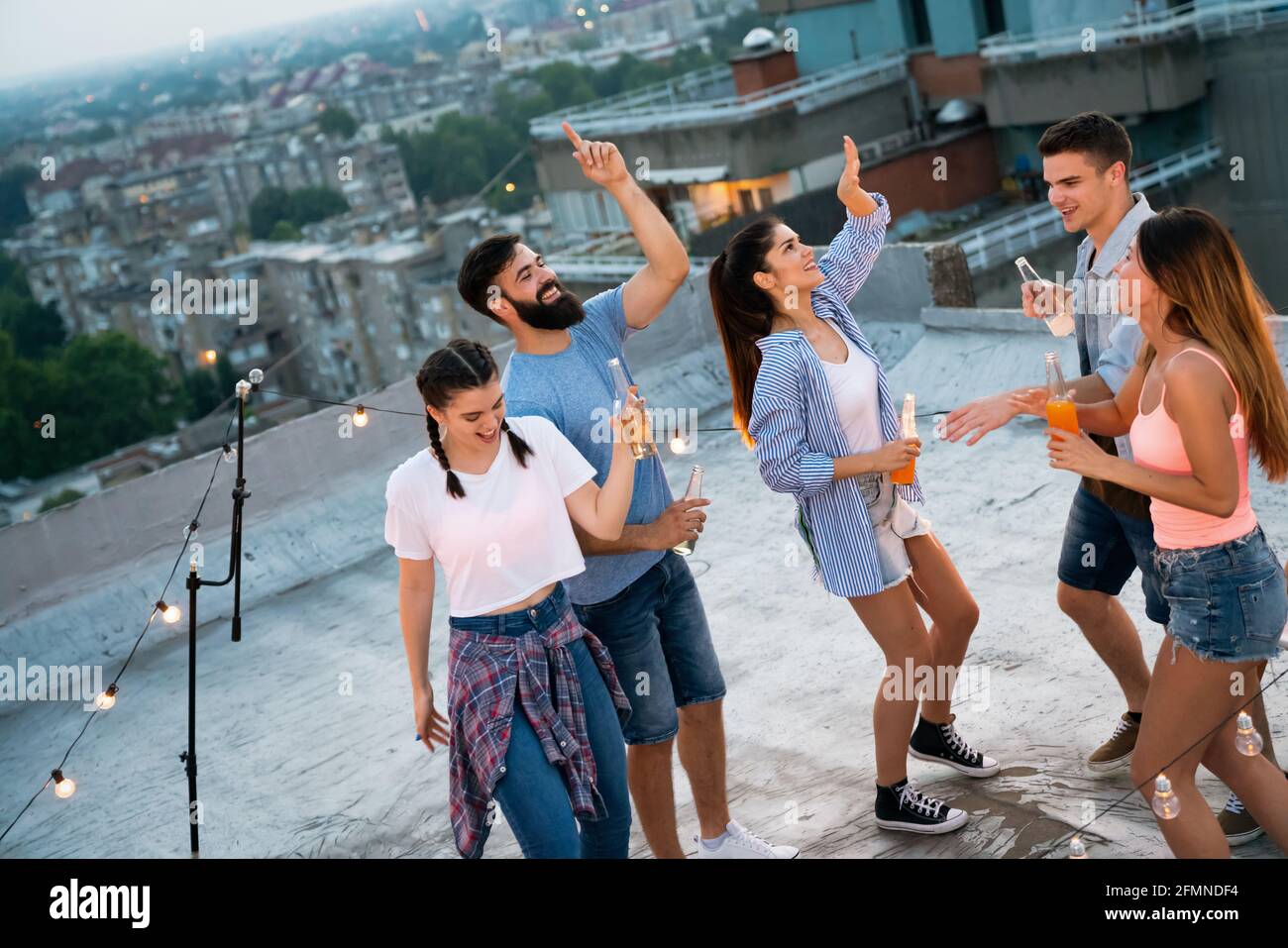 Friends enjoying cocktails at a party. Group of happy people having fun, dancing on a rooftop Stock Photo