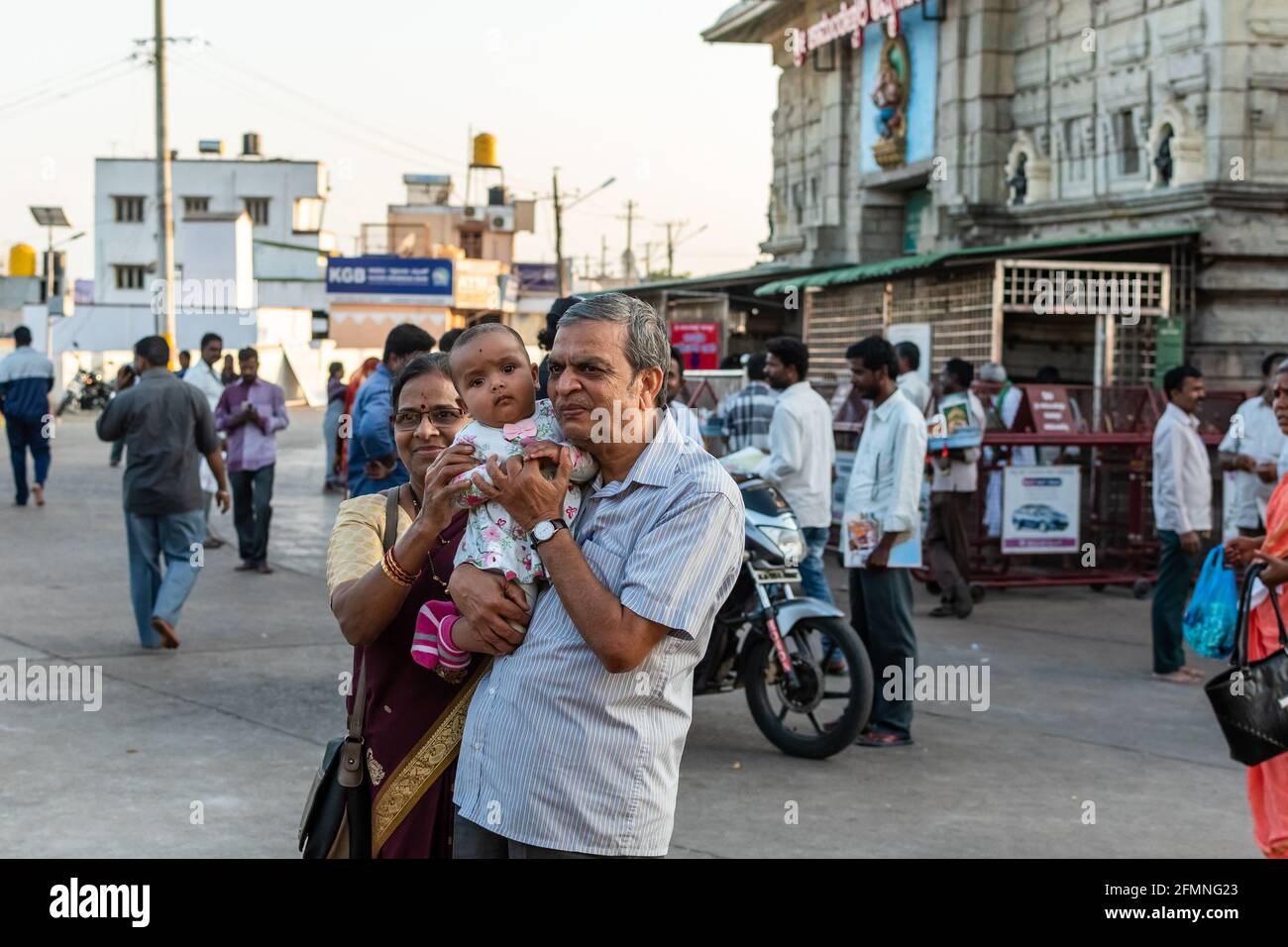 Mysore, Karnataka, India - January 2019: Two Indian grandparents holding a child and posing for a picture outside the ancient Chamundeshwari temple in Stock Photo