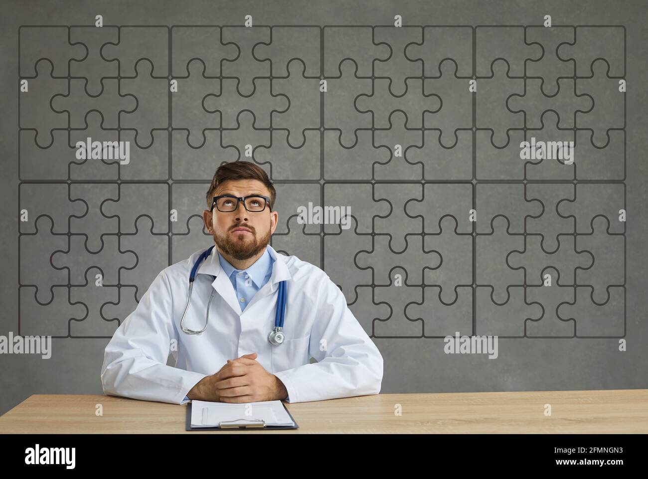 Doctor in lab coat sitting at desk and looking at background with complete jigsaw puzzle Stock Photo