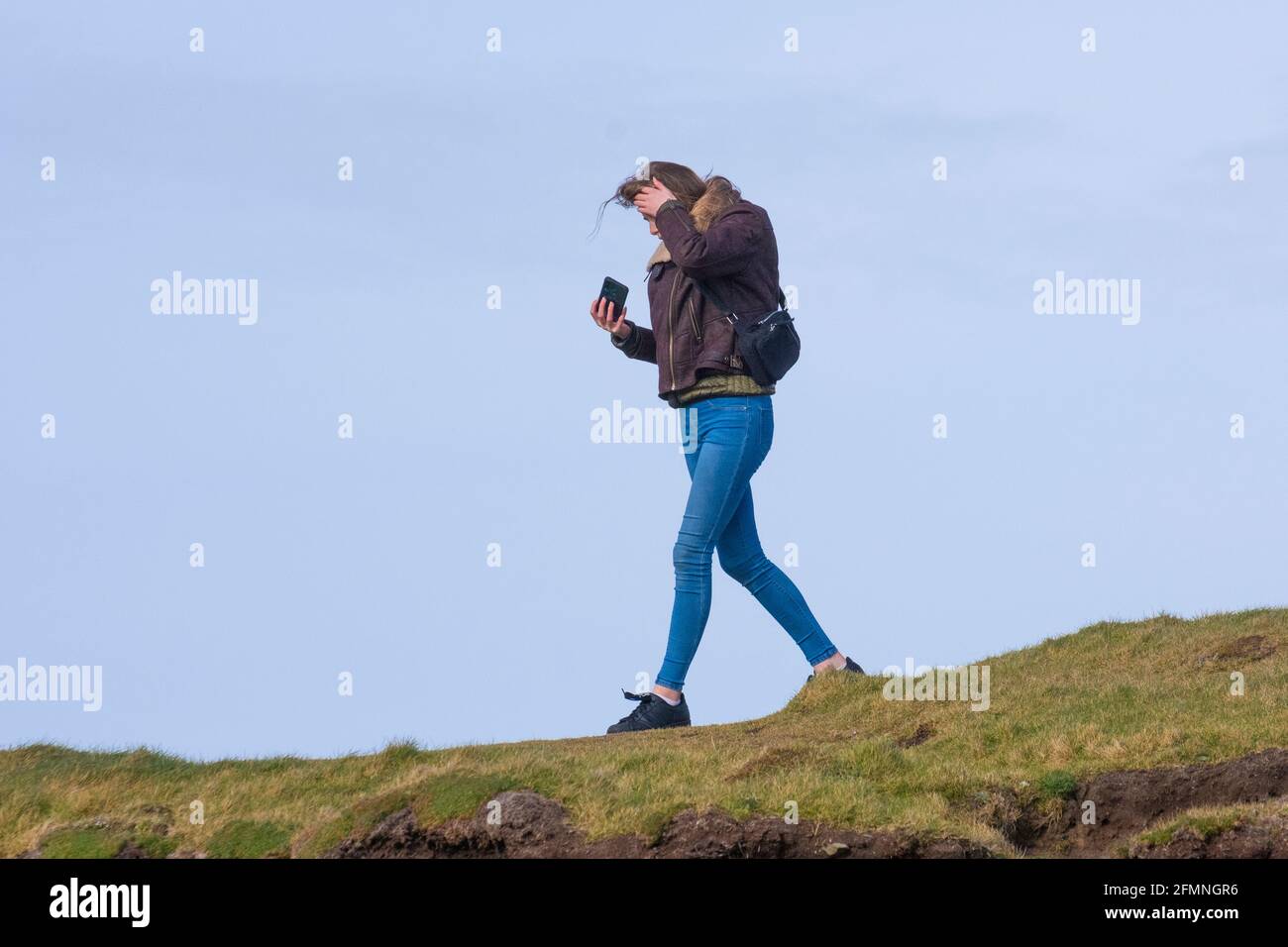 A young woman walking and looking at her mobile phone. Stock Photo