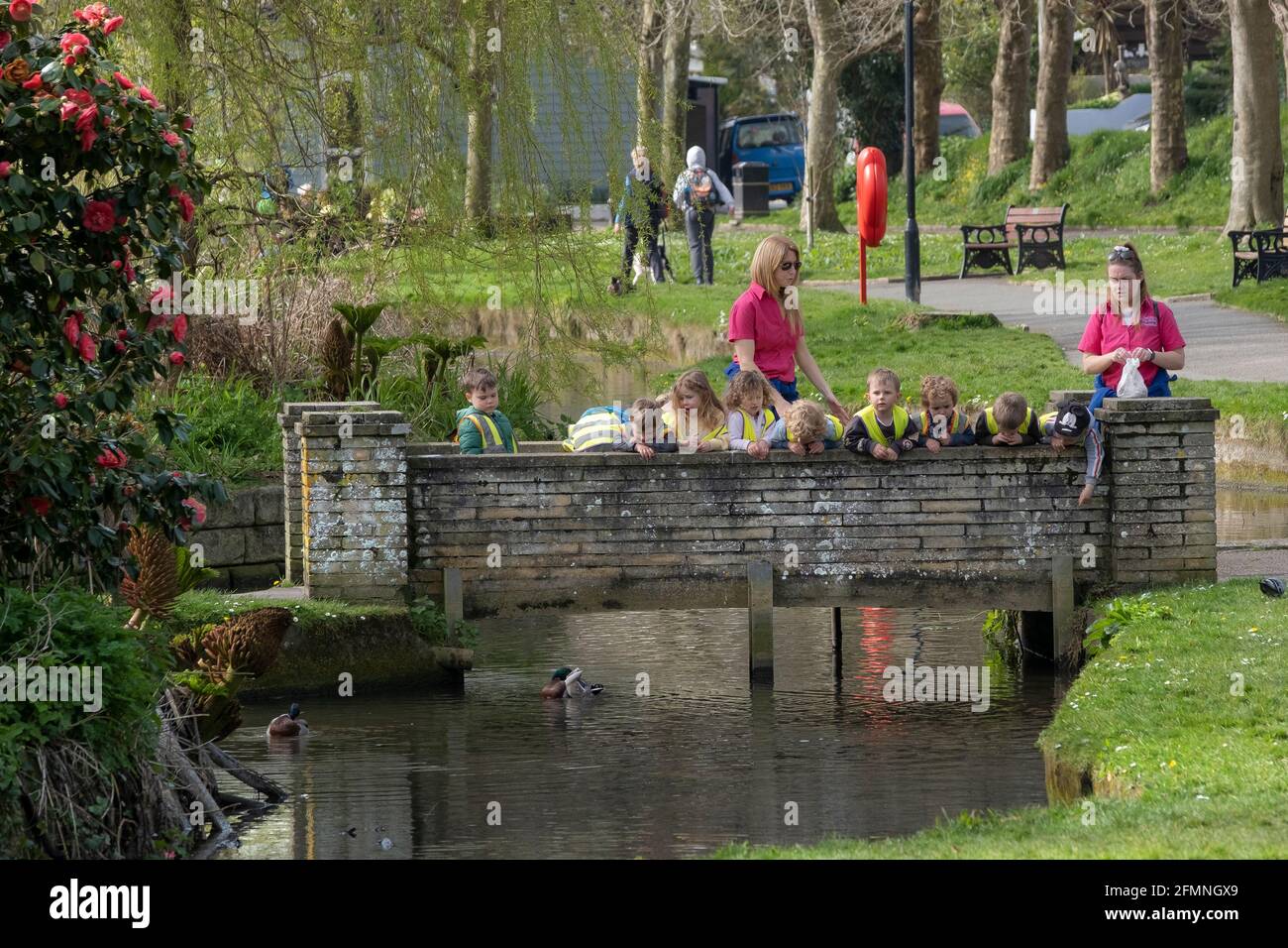 A group of young children from a pre-school nursery supervised by their nursery workers looking over a small footbridge at the ducks in Trenance Garde Stock Photo