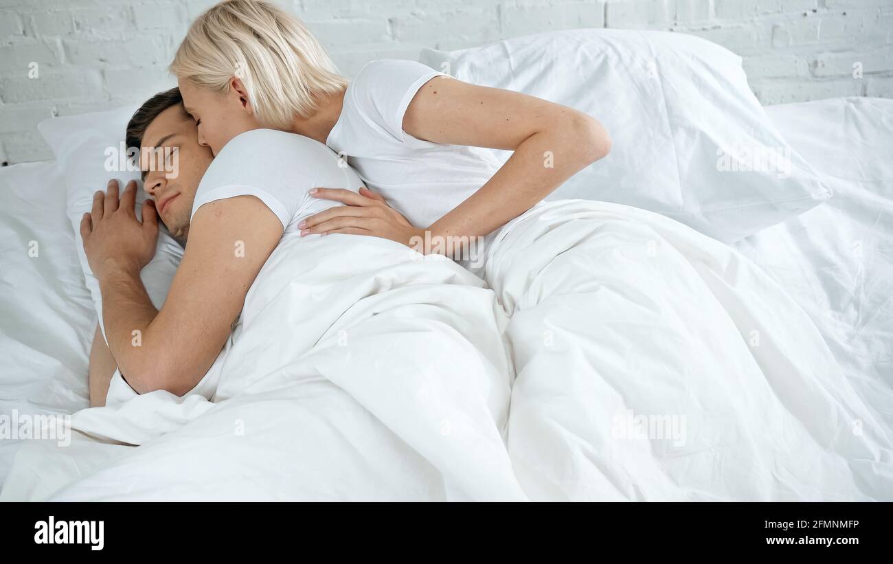 young woman kissing young man sleeping in bed Stock Photo - Alamy