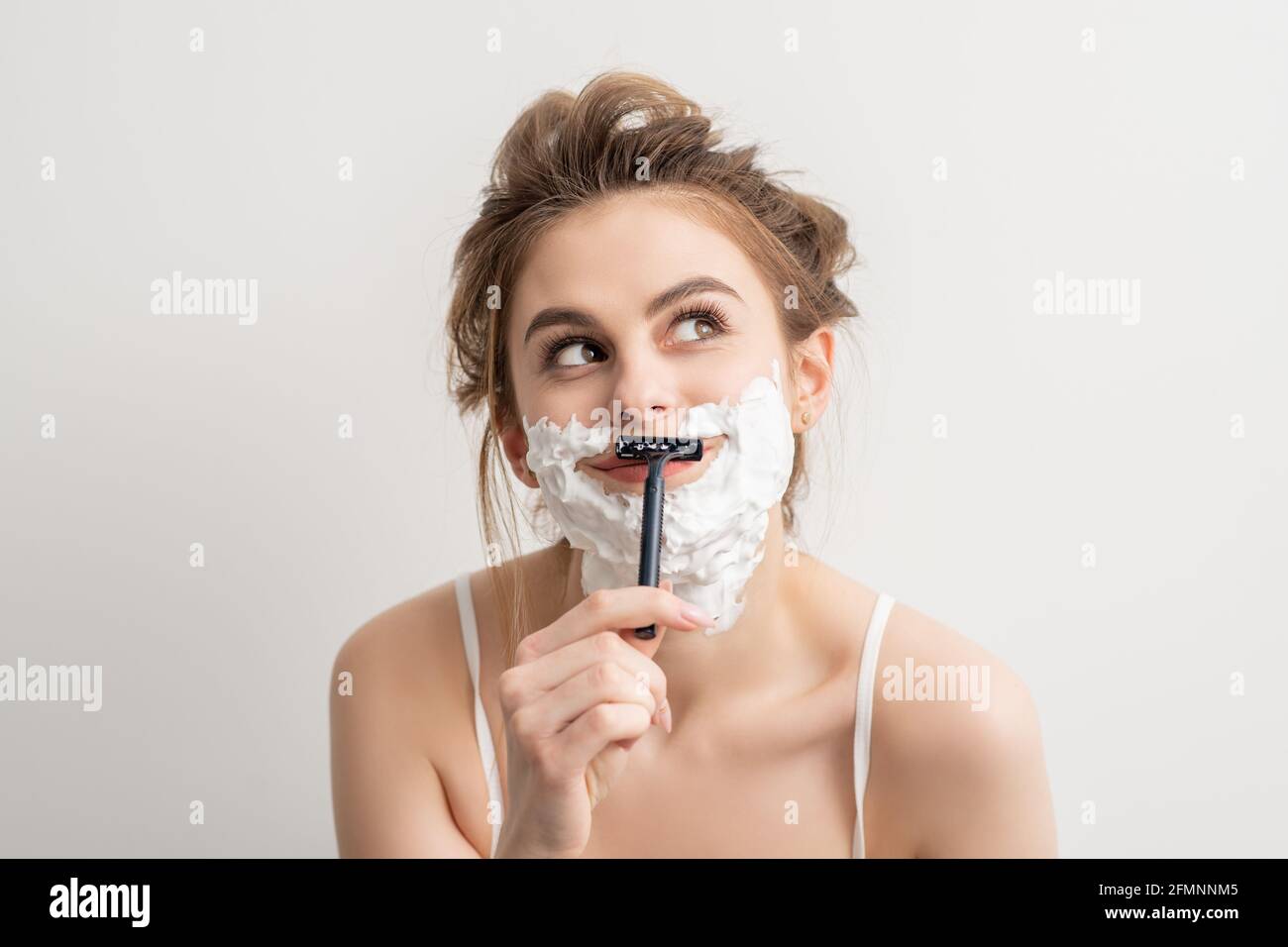 Beautiful young caucasian smiling woman shaving her face with razor