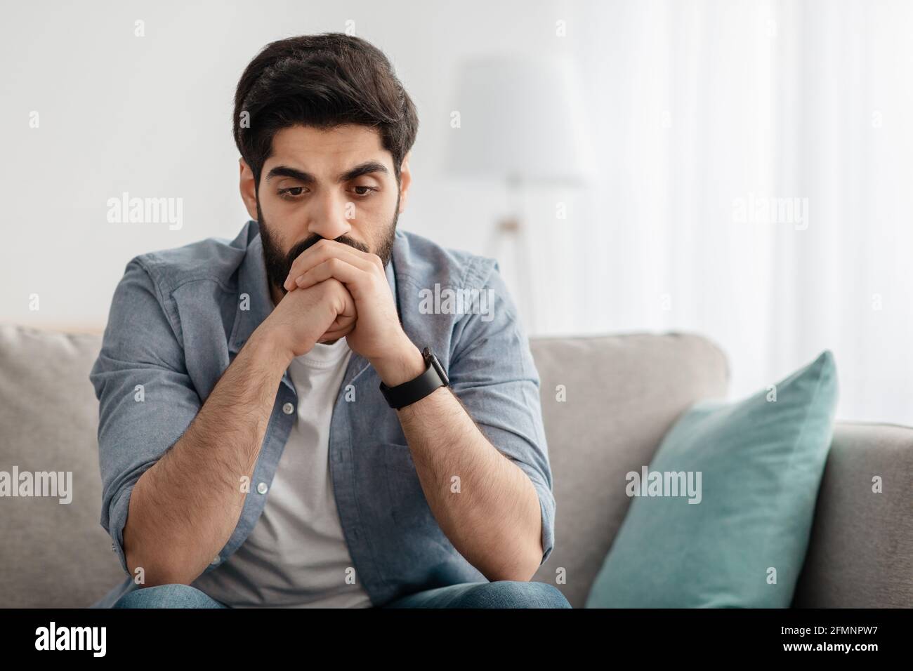 Depressed arab man having problems, thinking while sitting on couch at home, empty space Stock Photo
