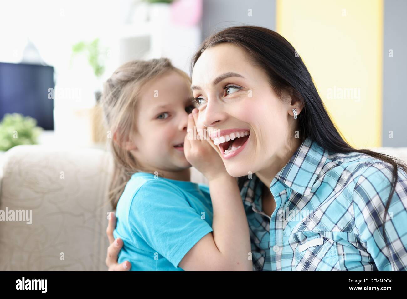 Little girl whispering secret to mom ear at home Stock Photo