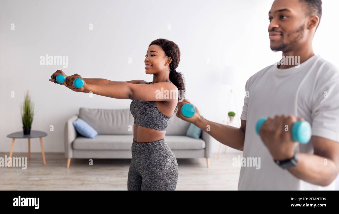 Positive African American couple exercising with dumbbells at home during covid-19 lockdown, panorama Stock Photo