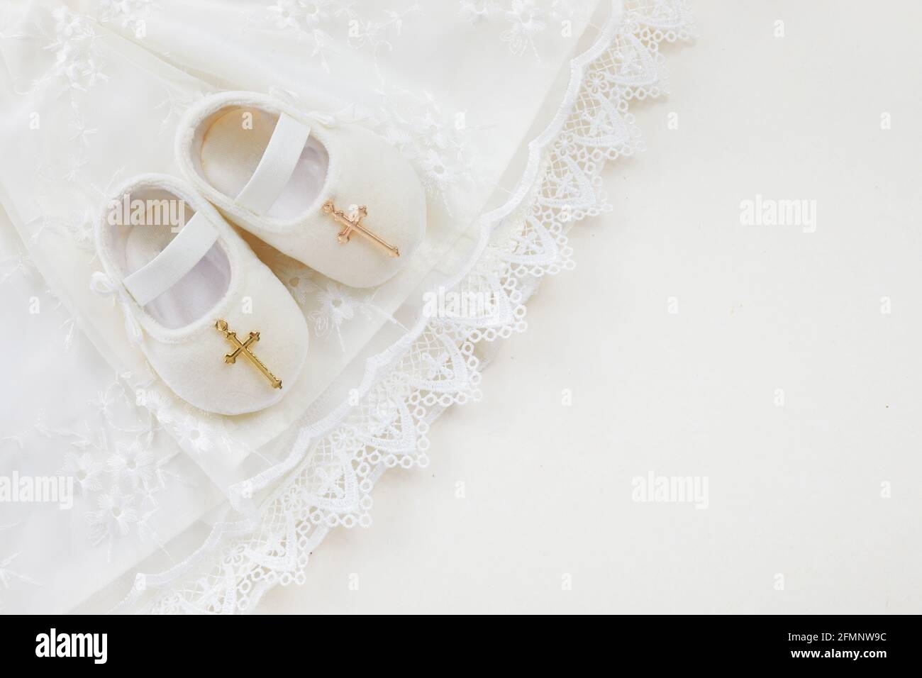 Christening background with baptism baby dress, shoes, and cross on pastel background Stock