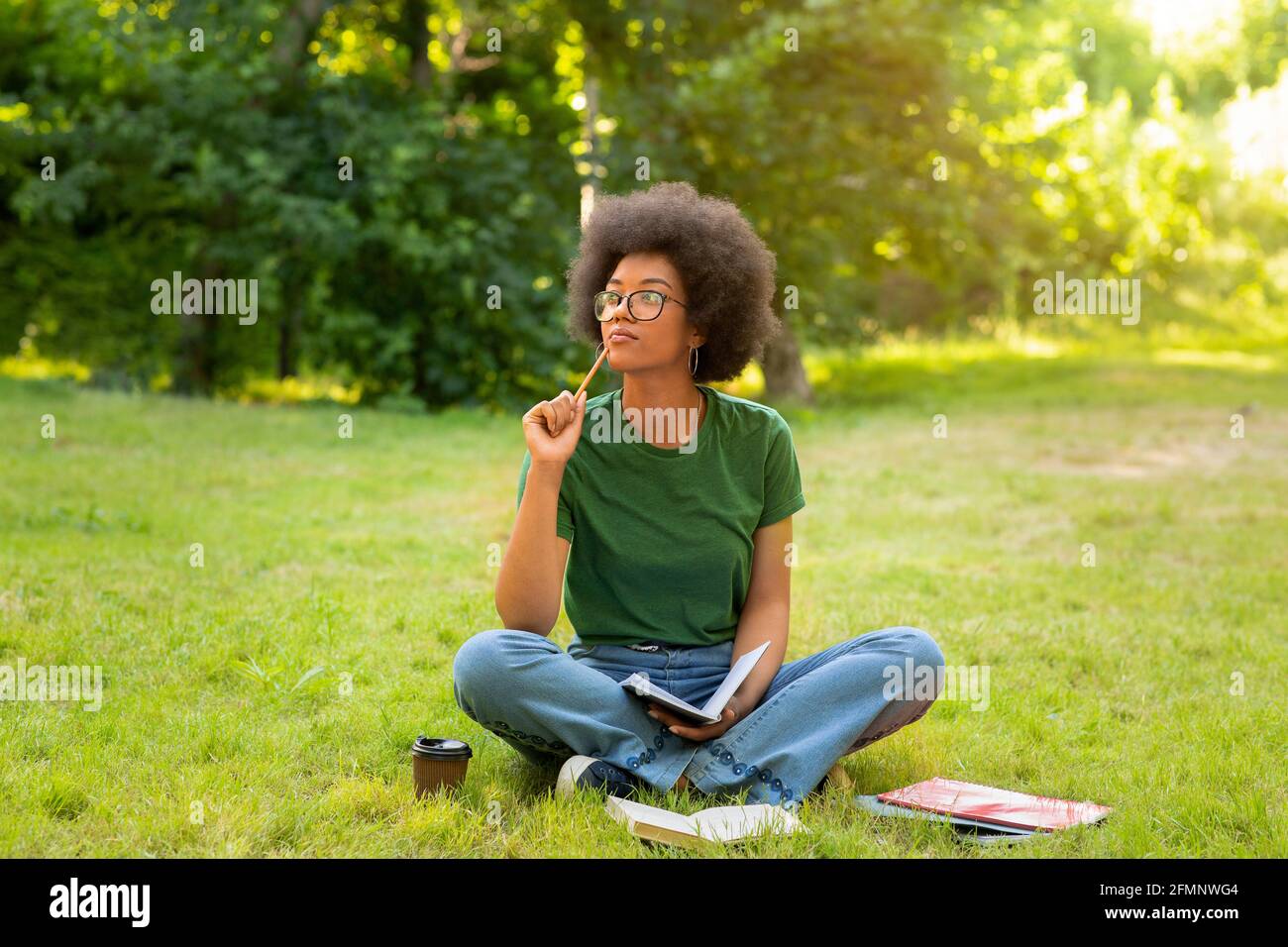 Thoughtful black student girl sitting outdoors, writing essay for college classes Stock Photo