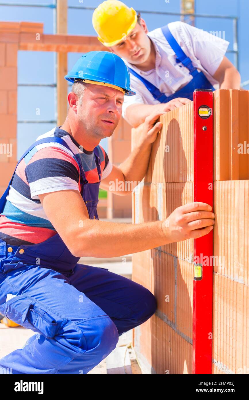 Construction site workers or bricklayer with helmets controlling building walls with a bubble level Stock Photo