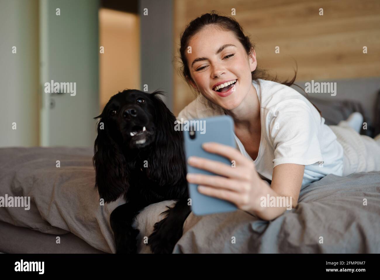 Smiling young brunette woman taking a selfie with her dog while laying ...