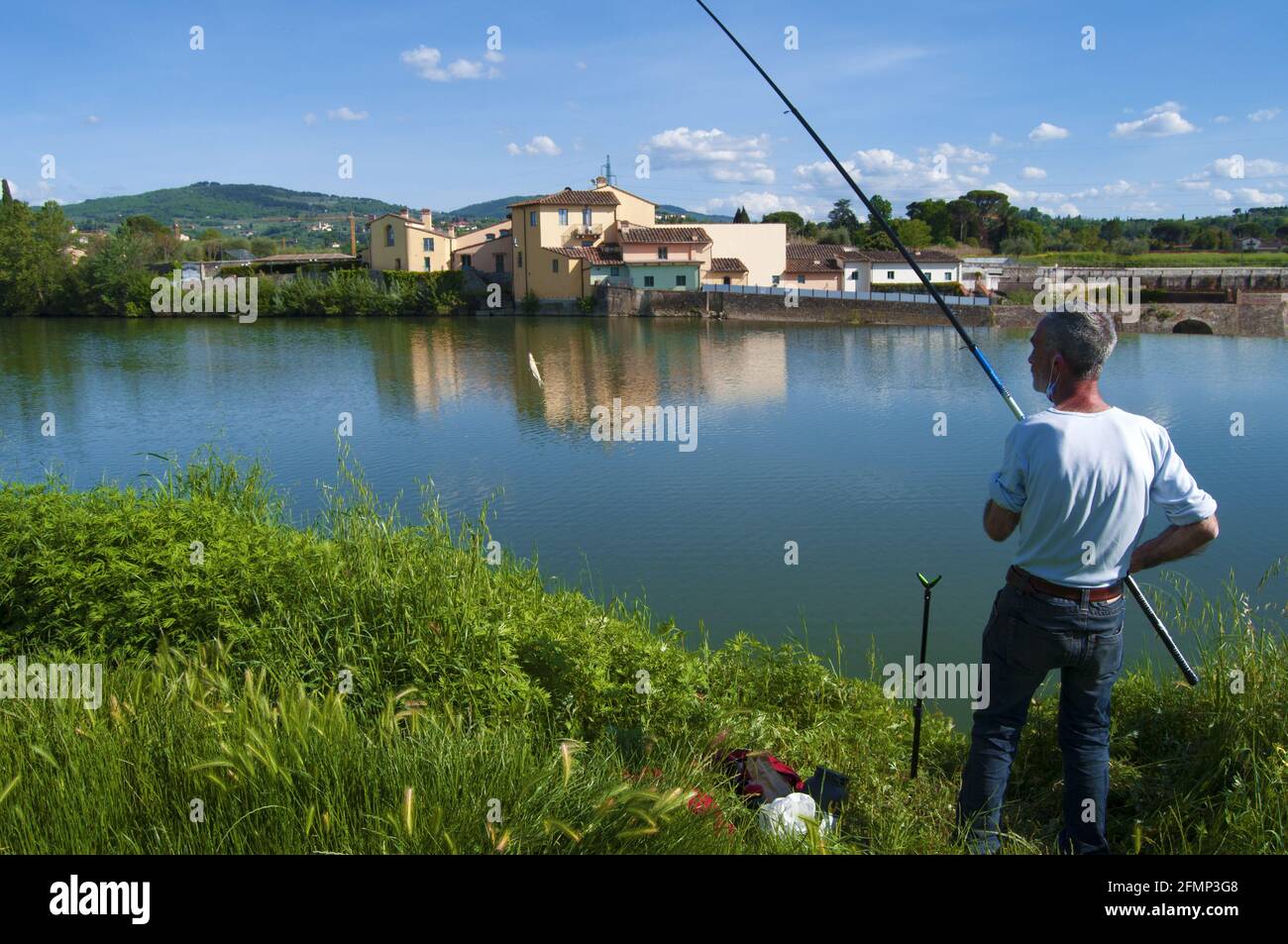 Florence, Italy - Fisherman on the bank of the Arno river, when he catches a small fish on the hook. Stock Photo
