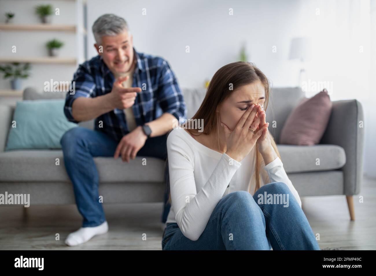 Mature woman sitting on floor and crying, her husband blaming or accusing her at home Stock Photo