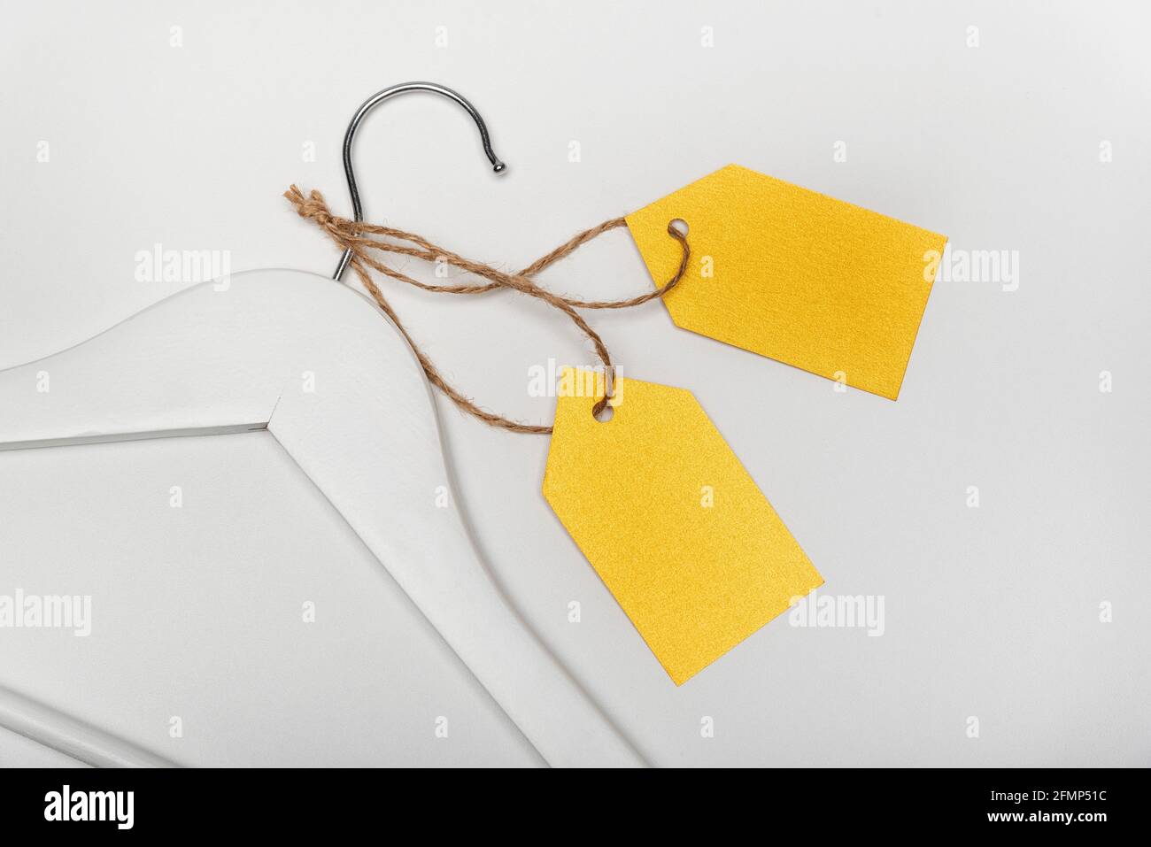 Wooden coat hanger with yellow paper labels, white background. Blank Label mockup . Clothing tag