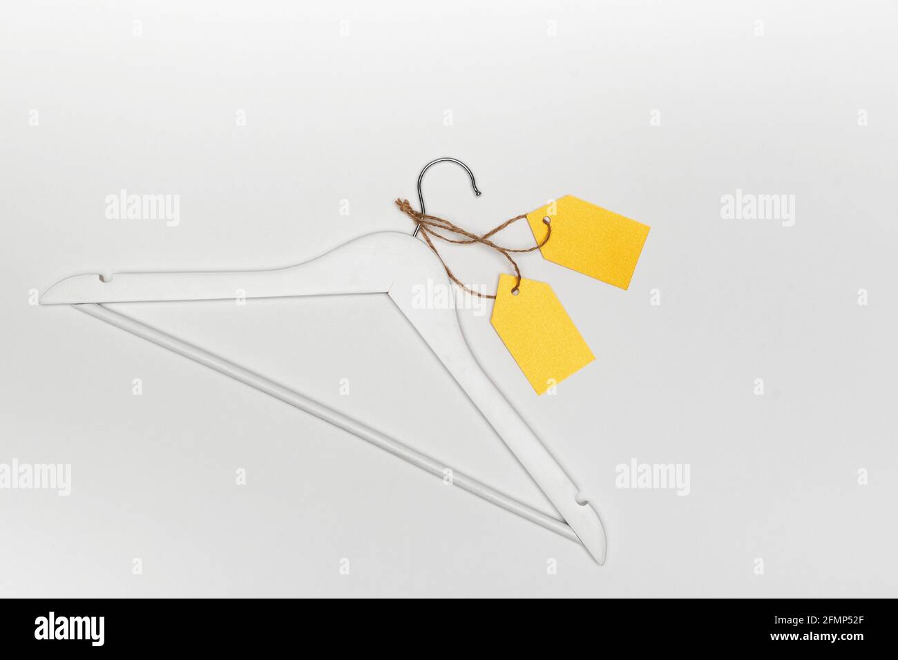 Wooden coat hanger with yellow paper labels on white background. Label blank mockup template. Clothing tag. Stock Photo