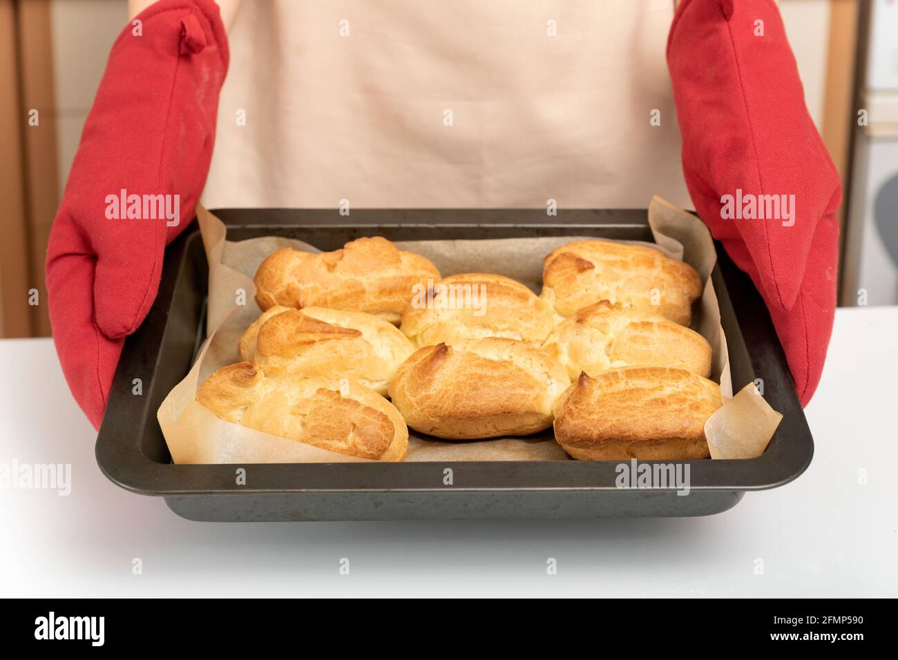 Cook in oven mitt holds baking sheet of scones. Profiteroles, puffs, popovers, eclair Stock Photo