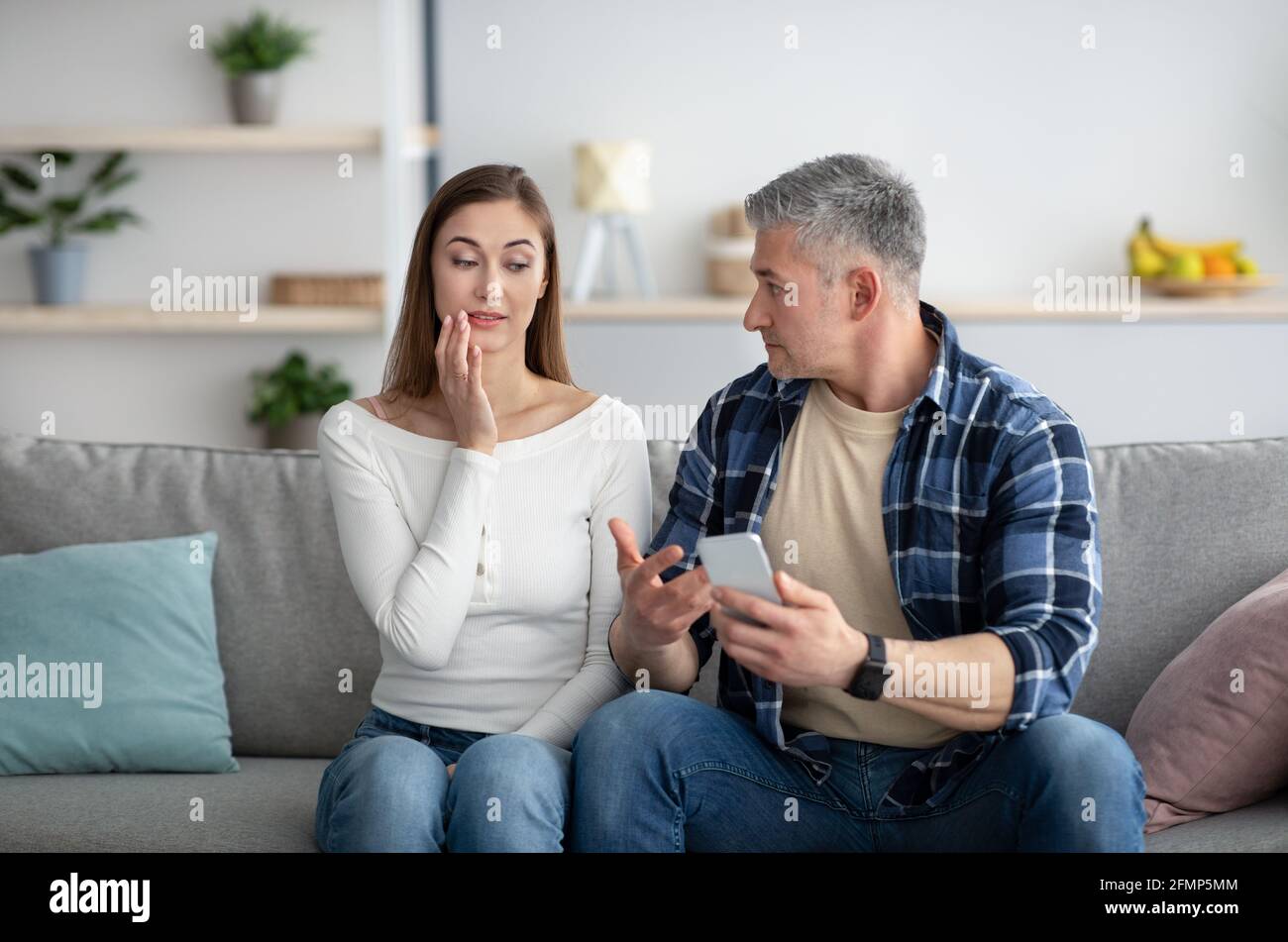 Mature man finding out about his wife's affair, confronting her about photos with lover on mobile phone Stock Photo