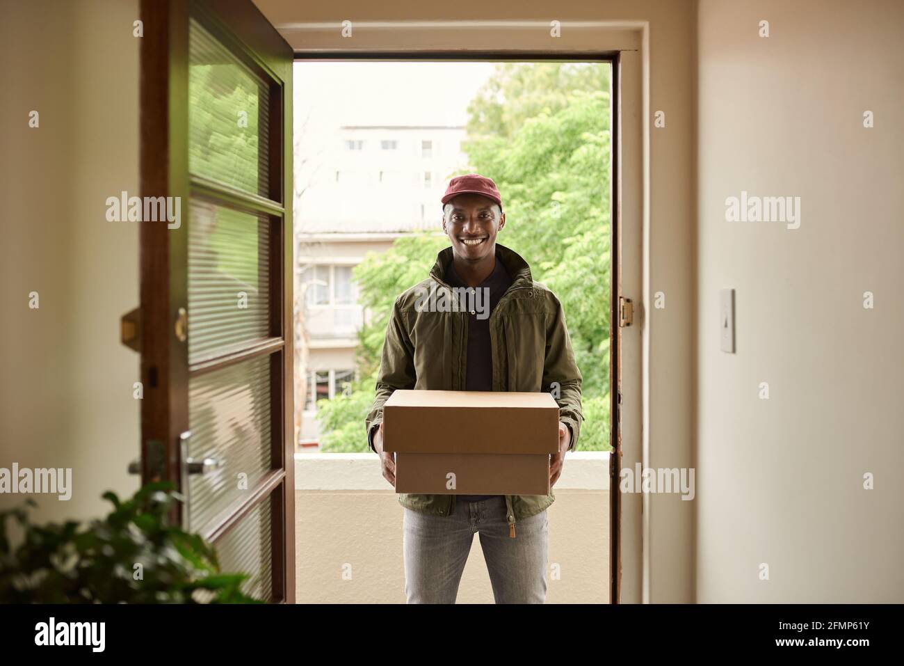 Smiling African delivery man standing at a front door carrying packages Stock Photo